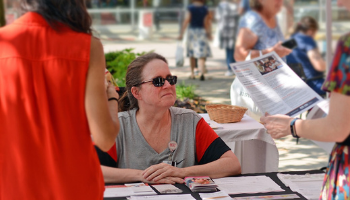 Librarian seated outdoors at a table smiling at two women looking at handouts