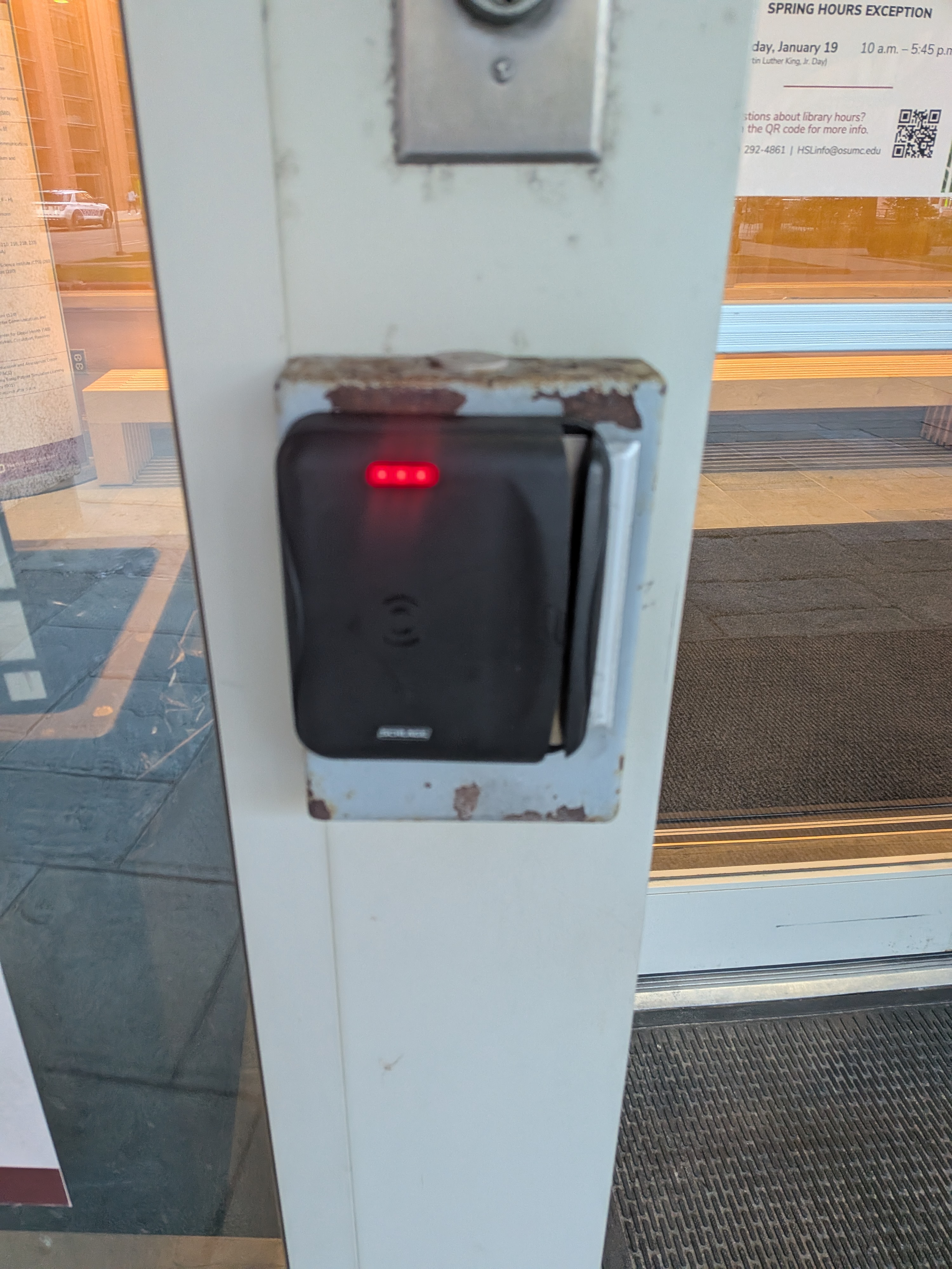 Tap-enabled Lenel card reader at the west main entrance of Prior Hall, mounted beside a glass door with red indicator lights.
