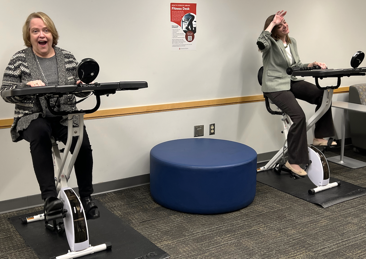 HSL director, Lynda Hartel (left), and HSL associate director, Judith Wiener (right), train for the biking challenge on two of the library's new FitDesk bicycle desks.