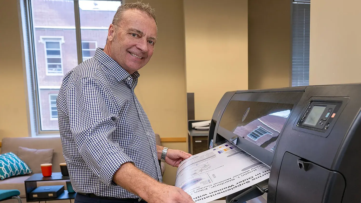 Man smiling while holding a poster that is in process of printing.