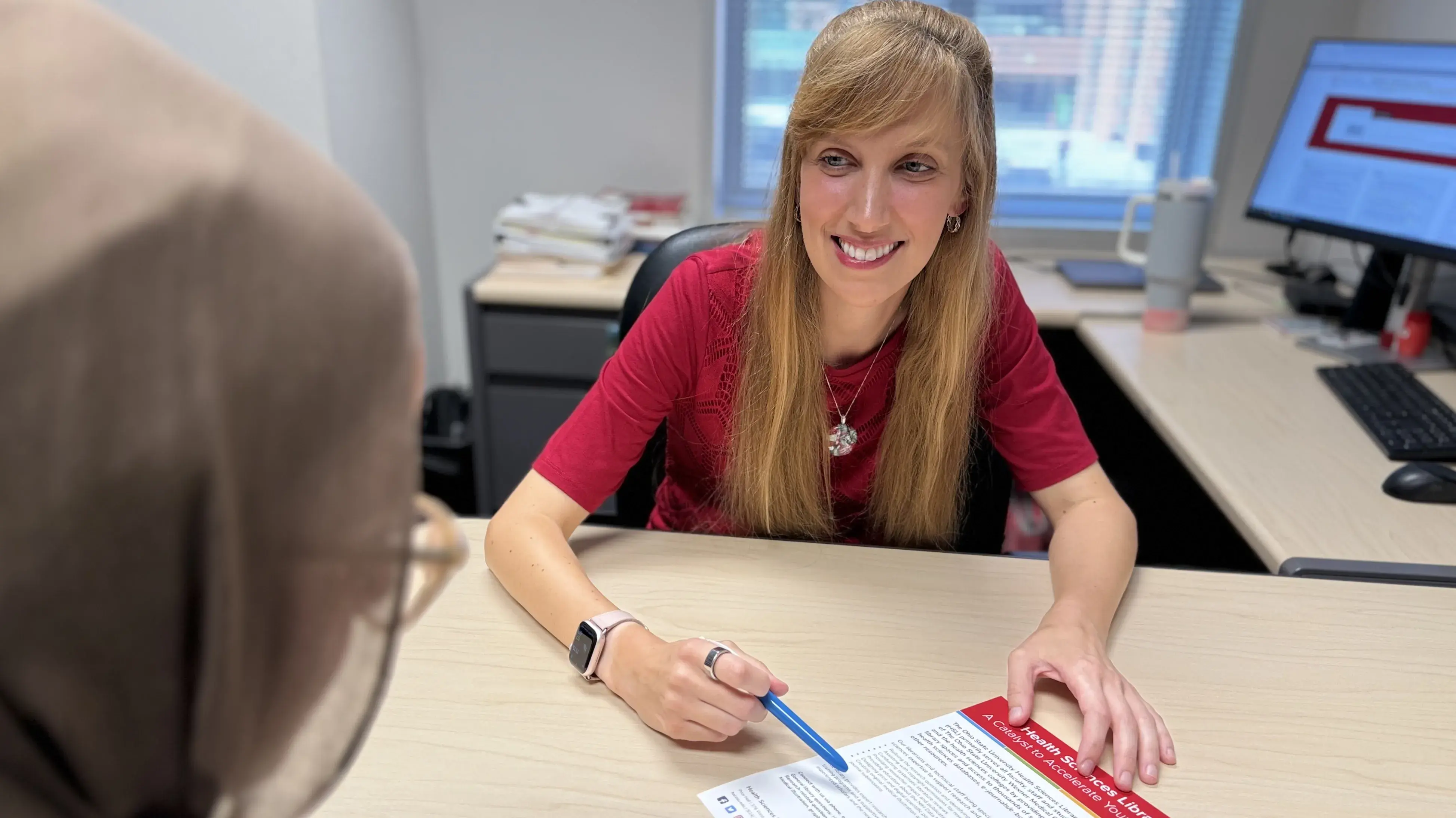A female librarian at a desk reviews a handout with a student