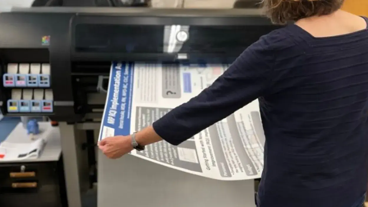 woman pulling a large poster out of a large format printer