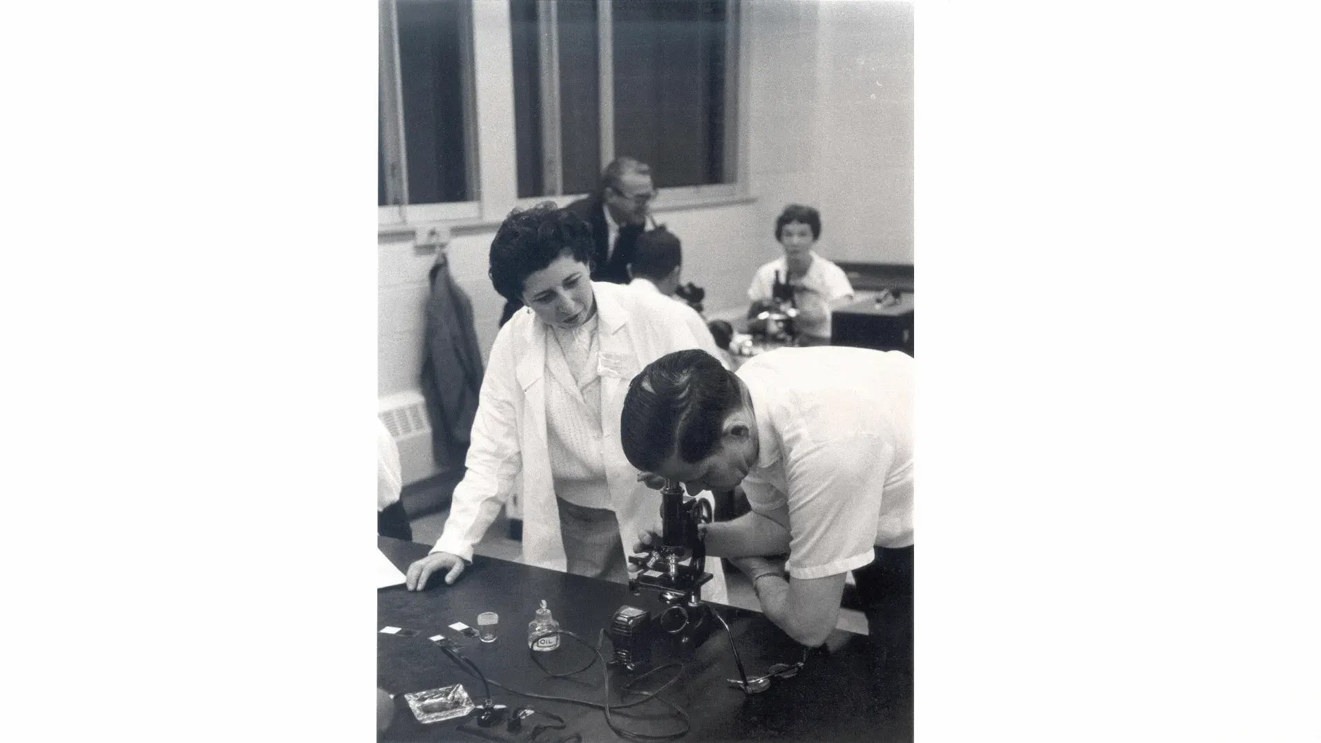 Bertha Bouroncle oversees a young man looking through a microscope in a classroom setting