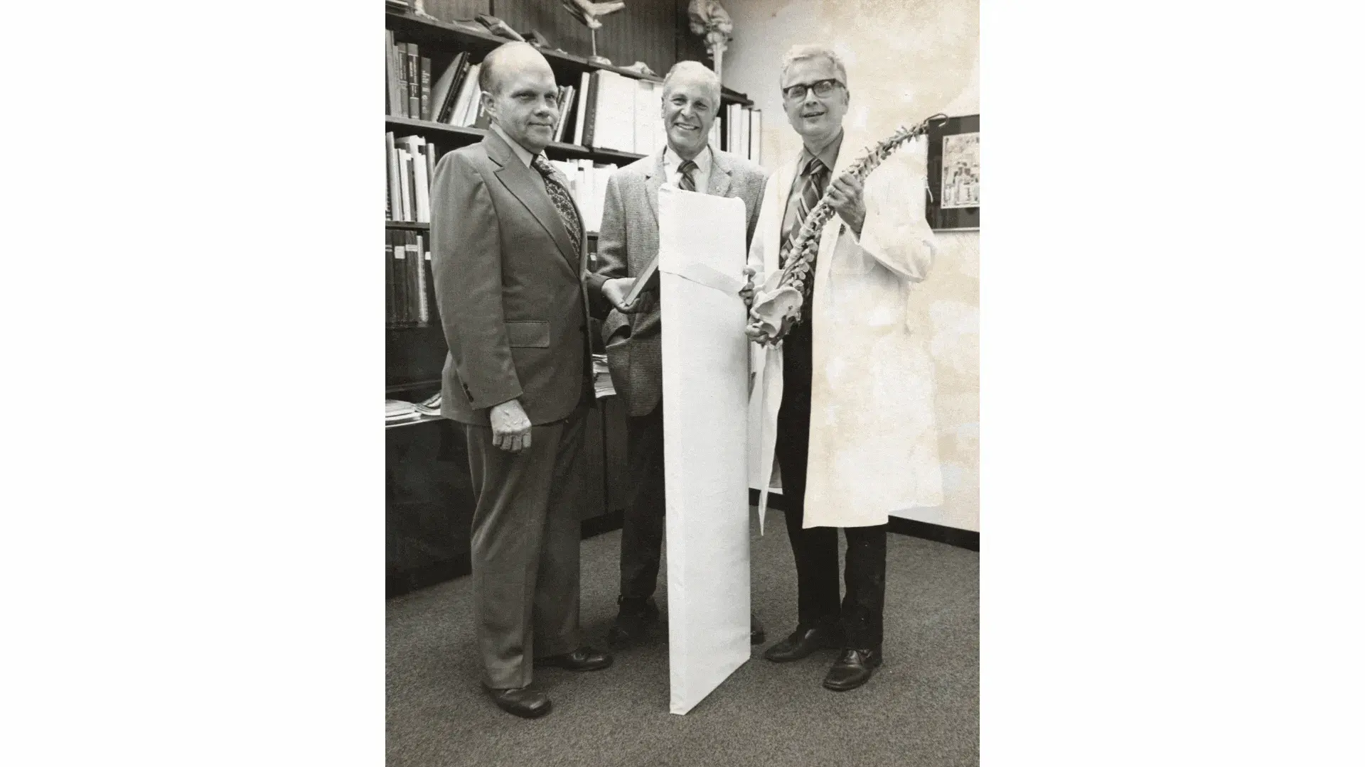 Ernest Johnson standing with colleagues, smiling while holding a model of a spine