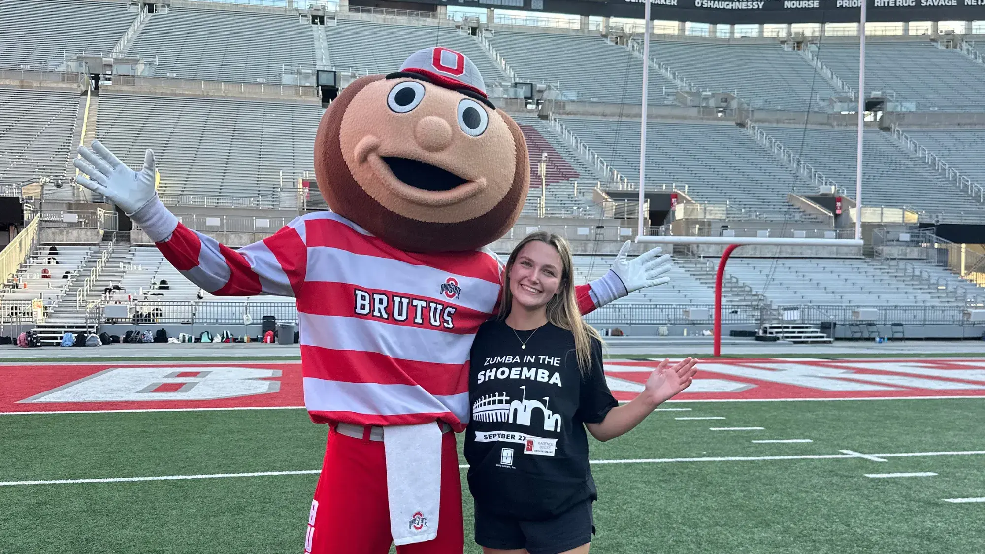 Kadence pictured with Brutus Buckeye, smiling on the football field.