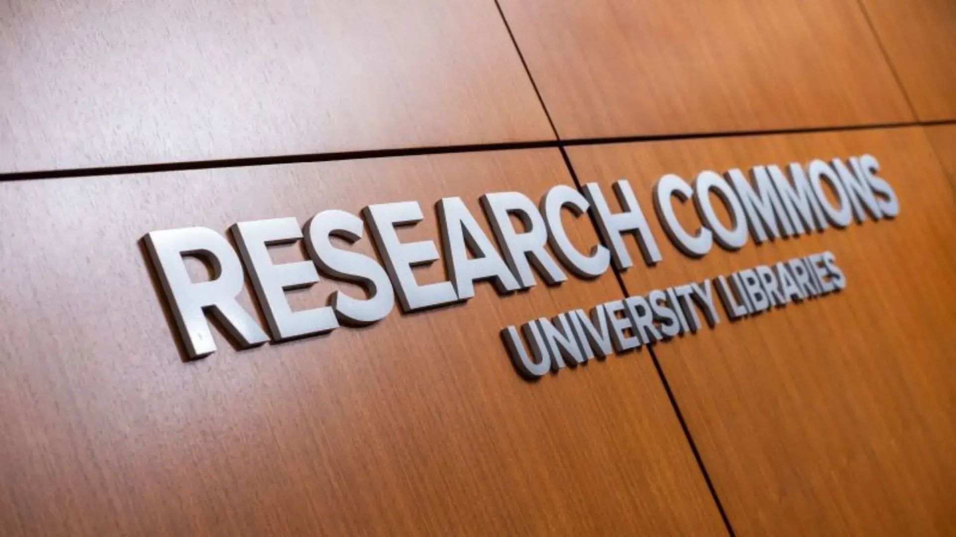Entrance sign for the Research Commons with the name and University Libraries against a wooden wall background