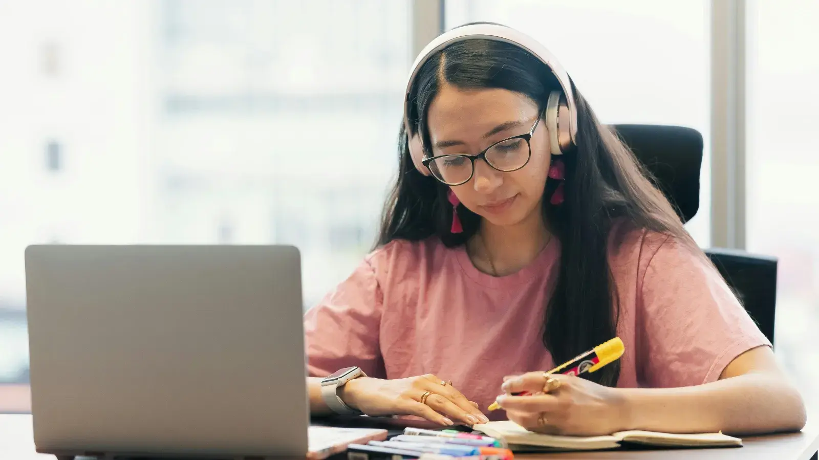 Woman with headphones, a laptop and book, studying.