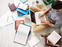 man sitting on floor with laptop surrounded by notebooks, textbooks and pencils