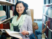 woman standing in library stacks holding a book