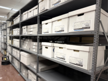 Metal shelves filled with neatly stacked white archival boxes in a well-organized storage room. The atmosphere is orderly and efficient.