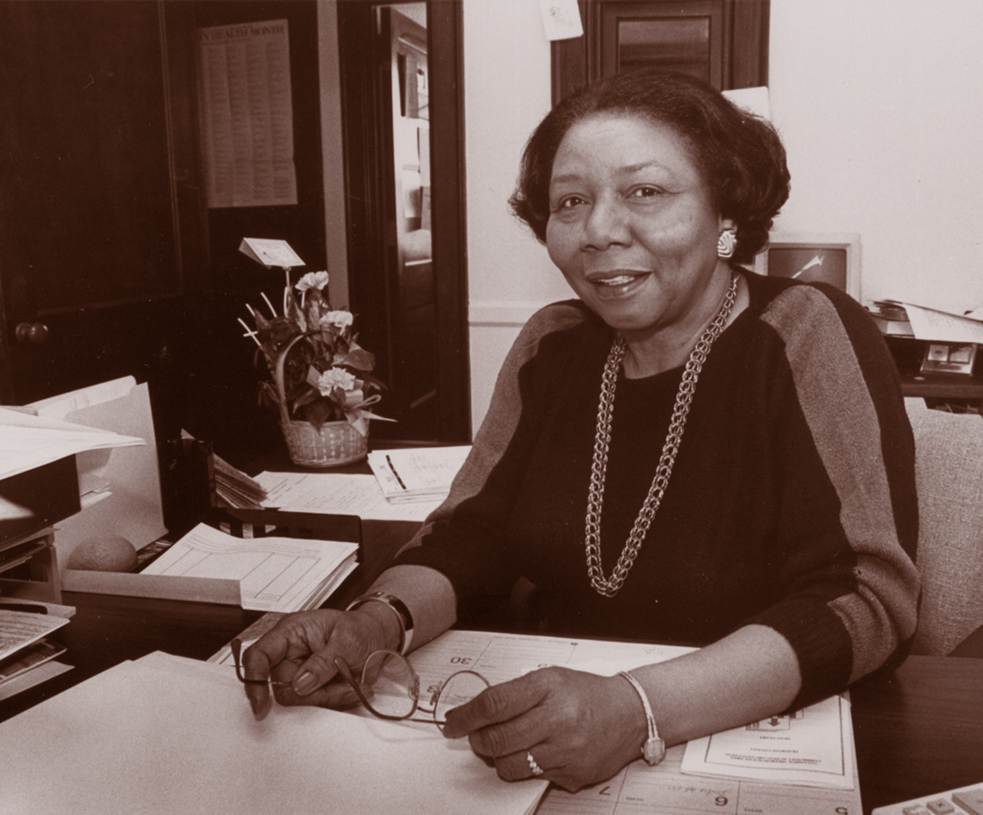 Portrait of Elsie Williams-Wilson, sitting at her desk smiling.