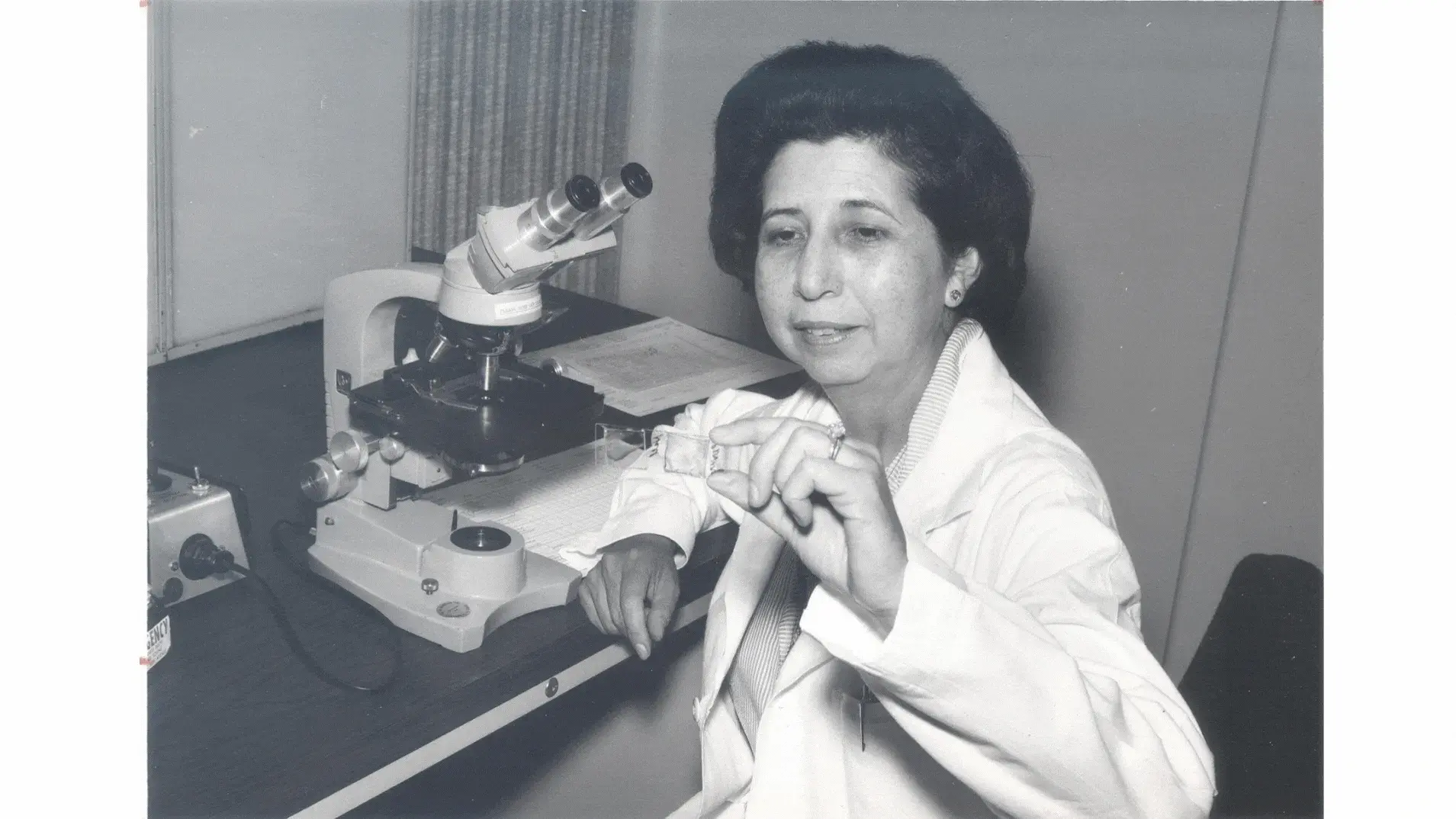 Bertha Bouroncle inspects a slide while sitting at her desk in front of a microscope